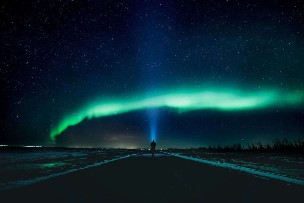 person standing in middle of a road in front of northern lights
