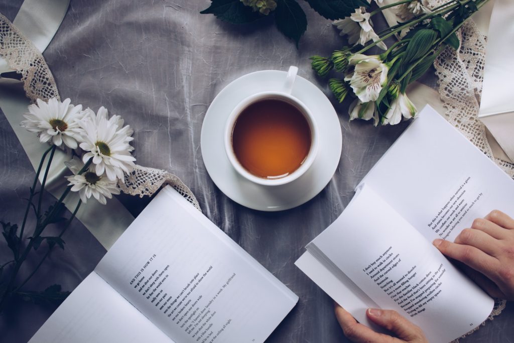 person reading poetry with cup of tea and flowers