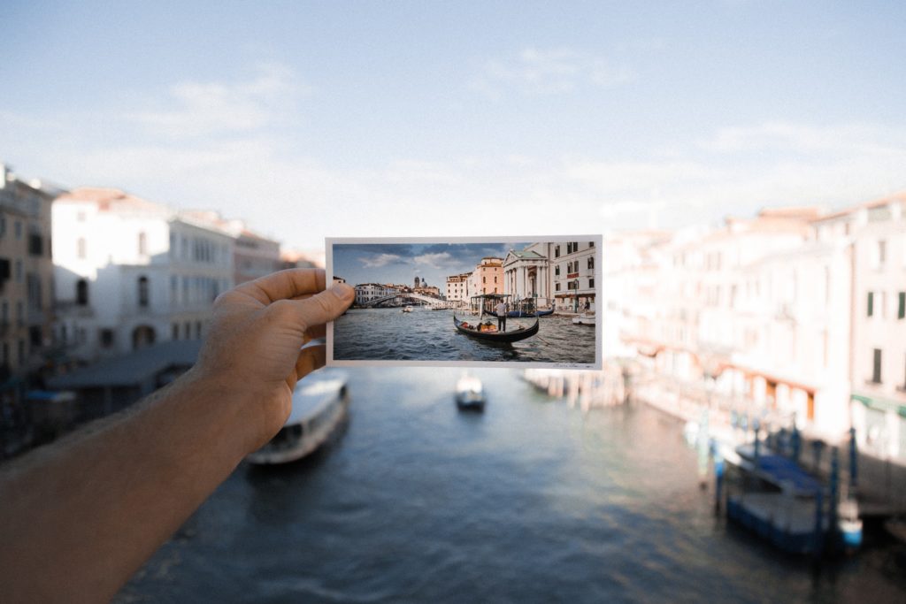 hand holding a photo of body of water in front of the same location