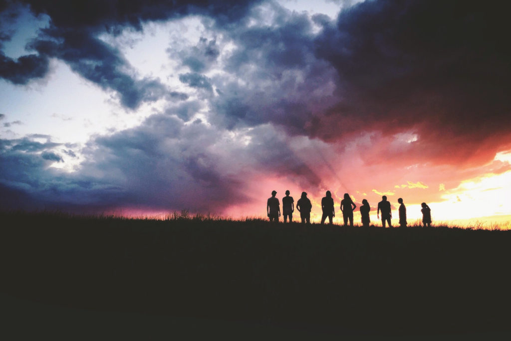 silhouettes of 9 people on a hill during a cloudy sunset