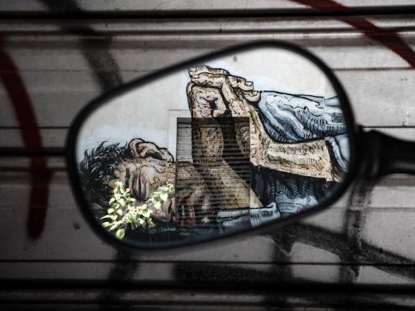reflection on a car mirror of street painting of man lying down