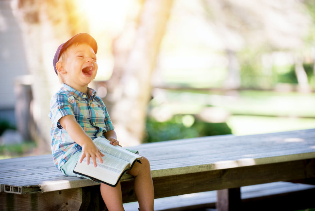 boy sitting on bench with a book laughing