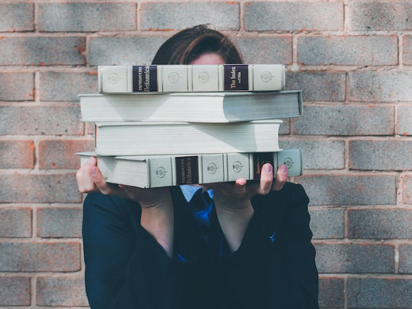 person holding stack of books covering face