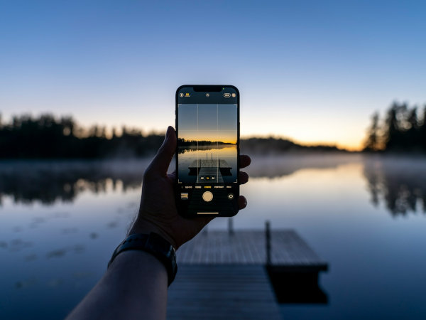 hand holding cell phone taking picture of a lake at sunset